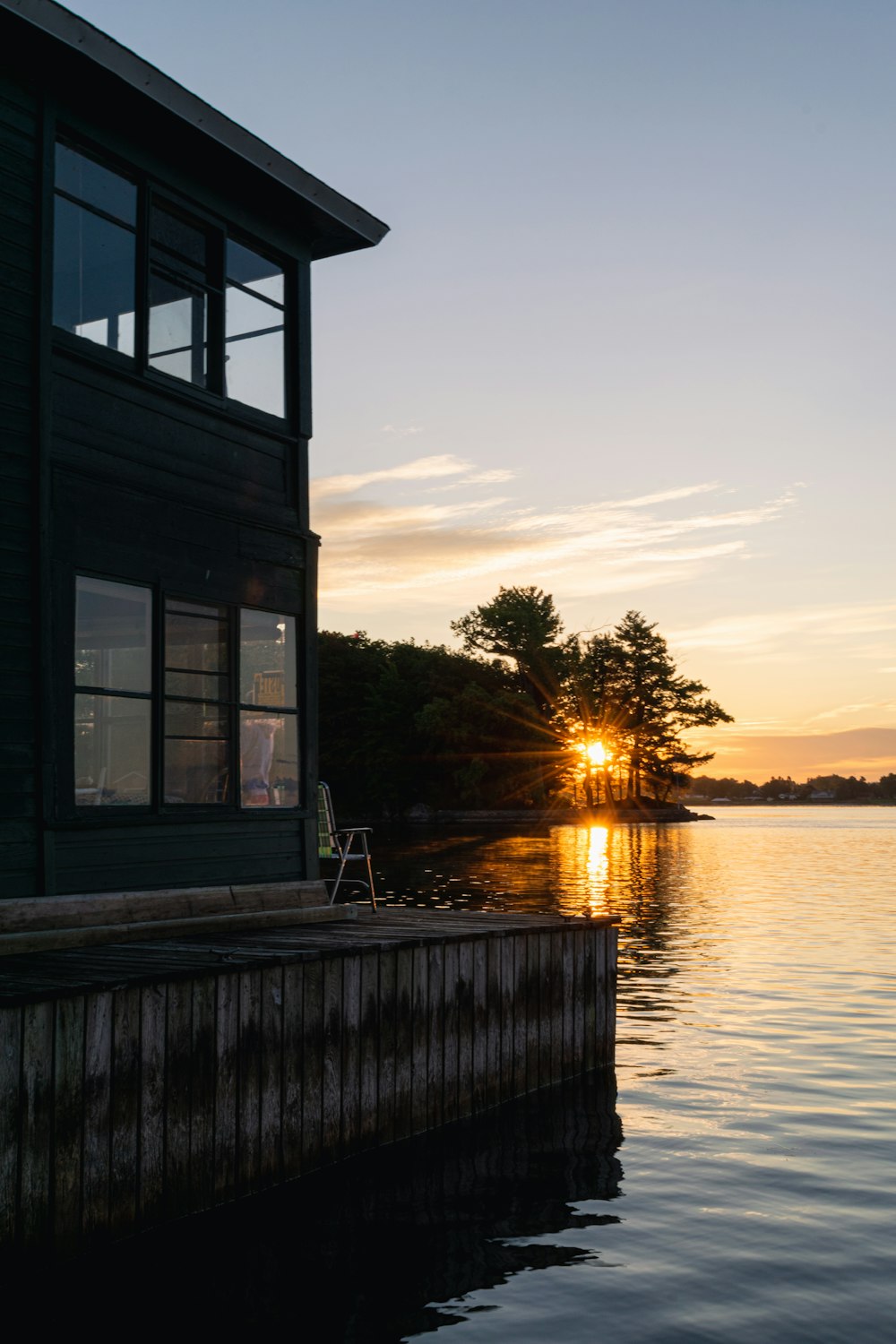 the sun is setting over the water near a house