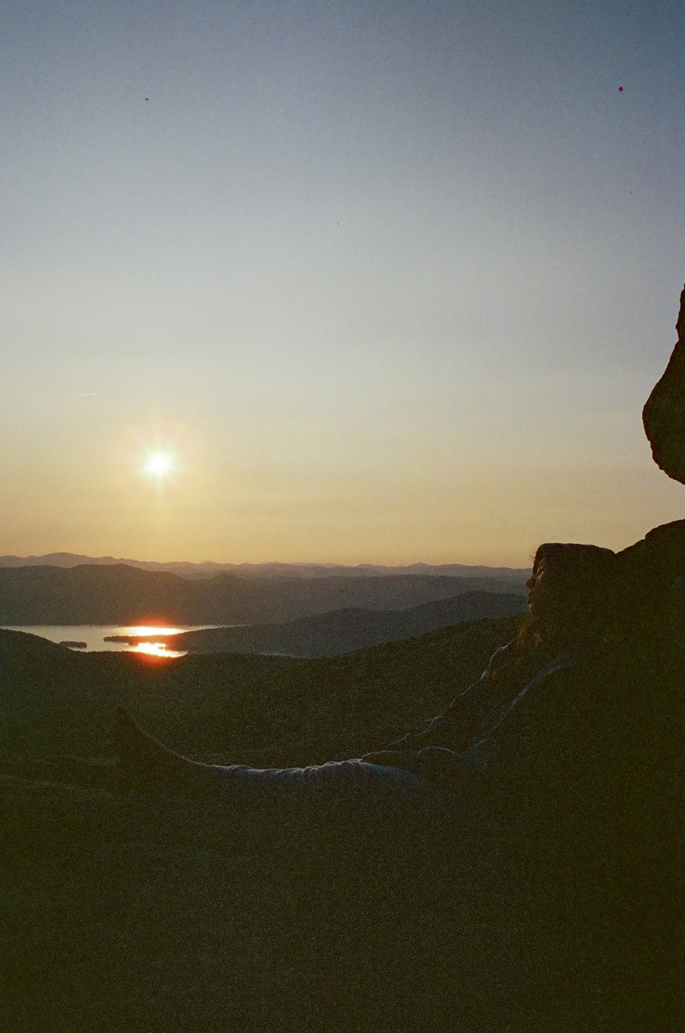 a person sitting on top of a hill with a sunset in the background