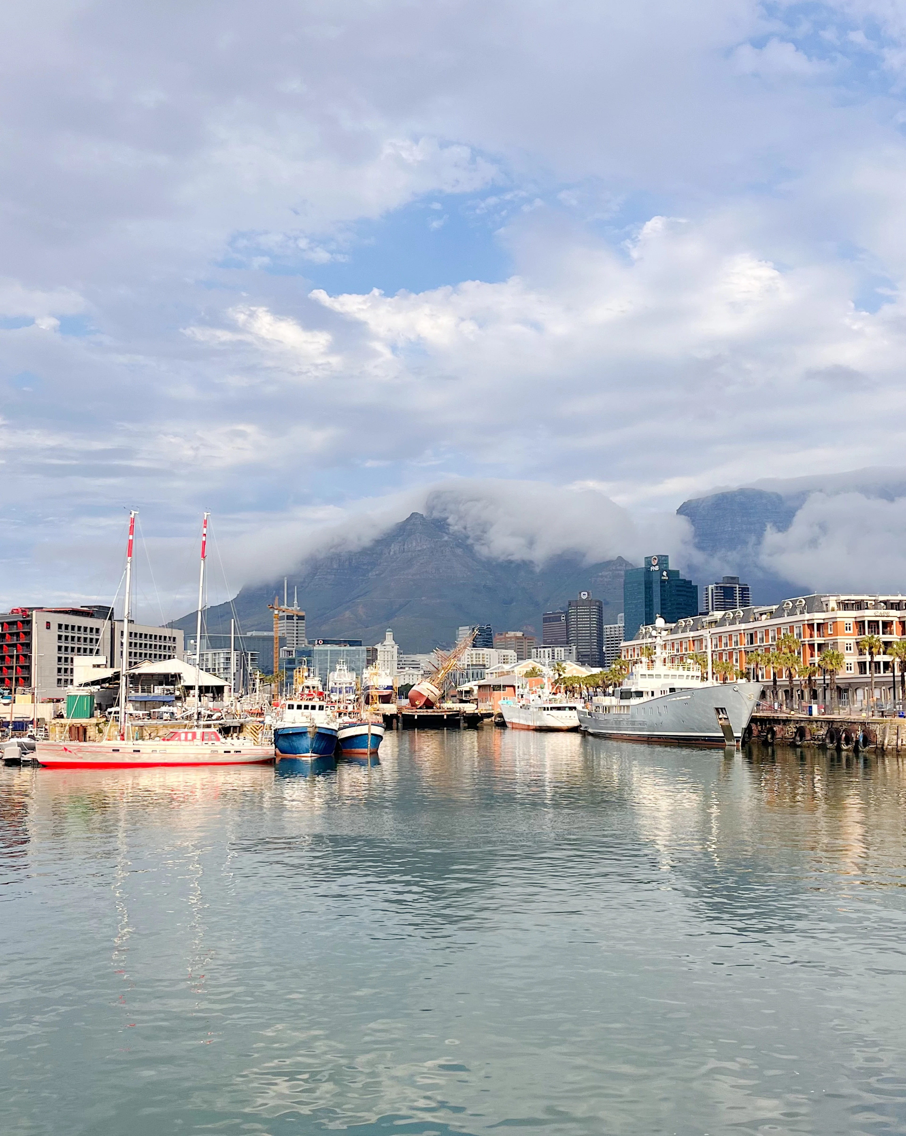 Colorful fishing boats moored at the Waterfront as clouds pour dramatically over Table Mountain.