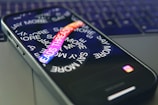 A smartphone lies on a laptop keyboard with the screen displaying swirling text that reads 'SAY MORE' and 'THREADS' in colorful letters. The Instagram logo is visible at the bottom of the phone's screen.