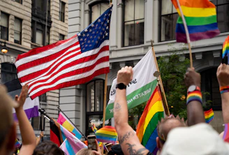 A vibrant street scene in a colorful gayborhood with rainbow flags and diverse community members enjoying a sunny day.