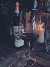 Rustic wooden table with a bottle of red wine and two glasses beside a lit fireplace.