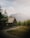 A rustic wooden cabin is nestled in a serene mountainous landscape, surrounded by lush green trees. The mountains in the background are partially covered with snow, and the sky above is filled with soft, fluffy clouds.