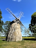 A rustic windmill standing tall over green pastures at sunrise.