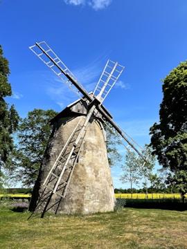 A rustic windmill standing tall over green pastures at sunrise.