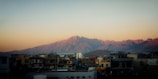 Residential buildings in the foreground with a scenic backdrop of rugged mountains bathed in the soft light of either sunrise or sunset.