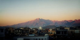 Residential buildings in the foreground with a scenic backdrop of rugged mountains bathed in the soft light of either sunrise or sunset.