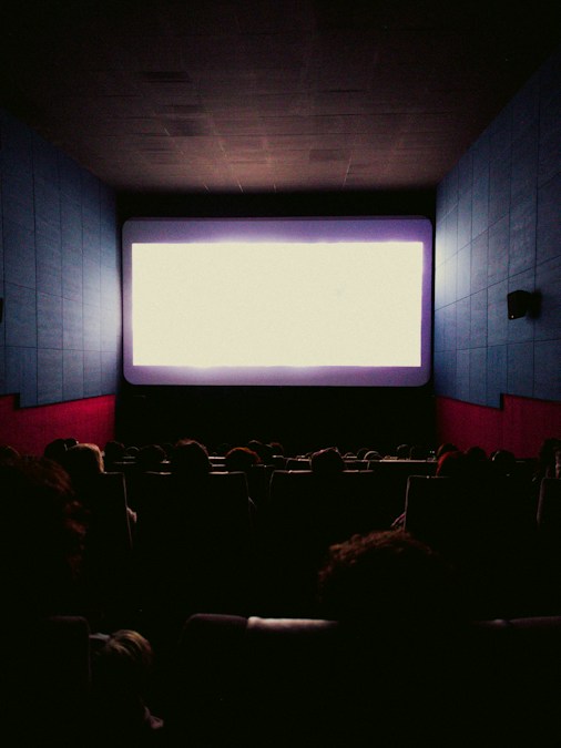 Spectateurs de dos dans une salle obscure face à un grand écran lumineux, à l'image des séances du FIFF de Namur