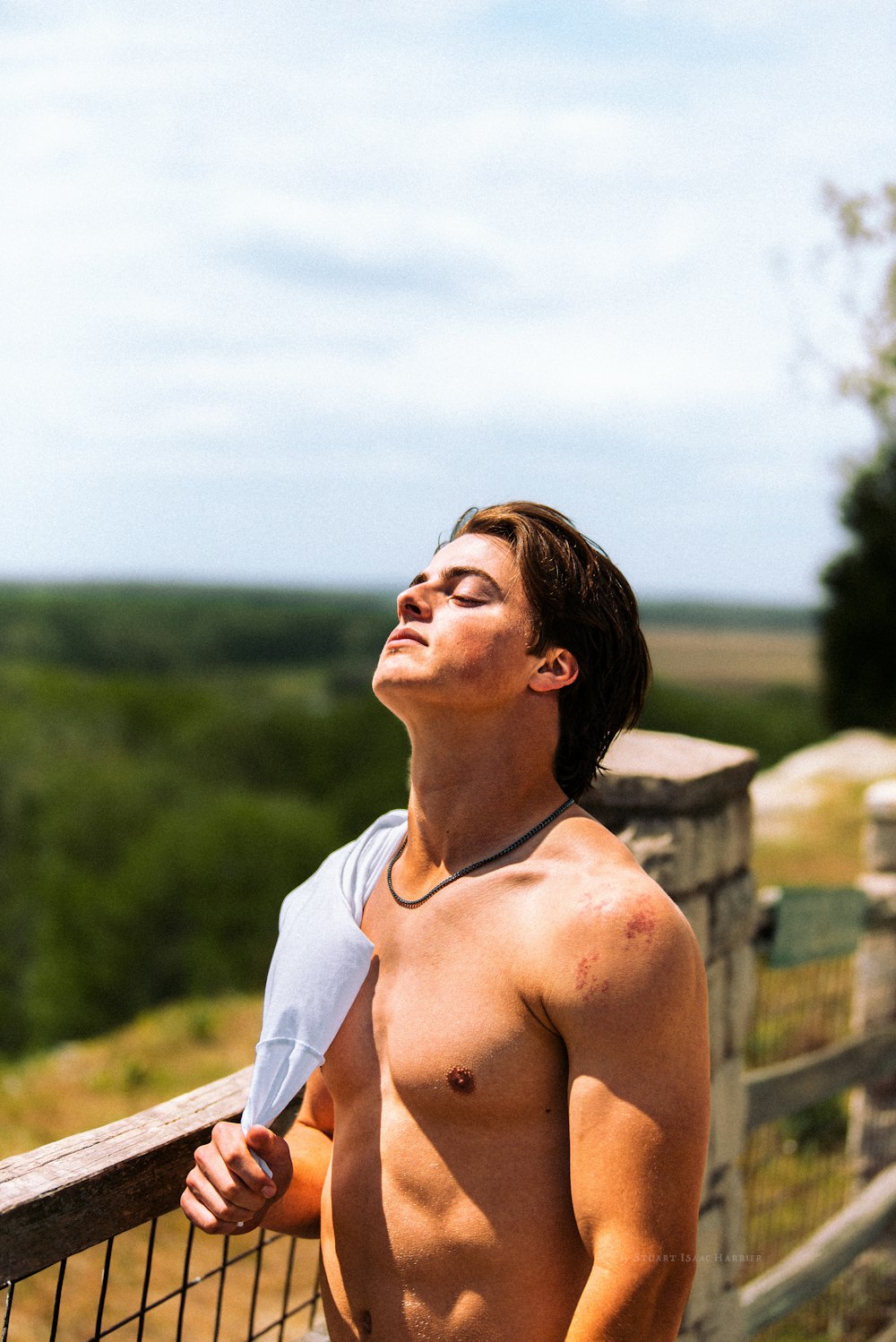 a shirtless young man standing next to a fence