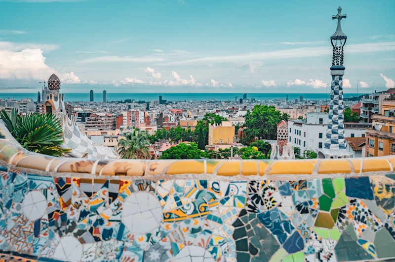 Park Güell's curving mosaic bench in the foreground with Barcelona's rooftops and the Mediterranean stretching to the horizon