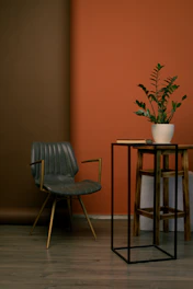 A serene living room corner featuring a stone beige armchair, antique gold accents, and a chic black vase on a minimalist side table.