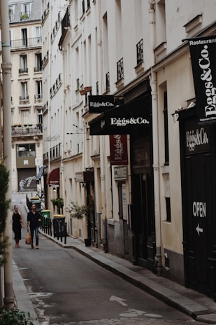 a couple of people walking down a street next to tall buildings