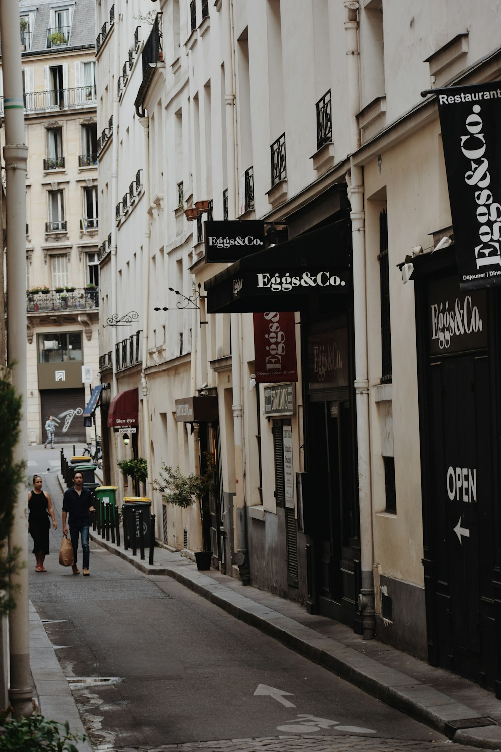 a couple of people walking down a street next to tall buildings