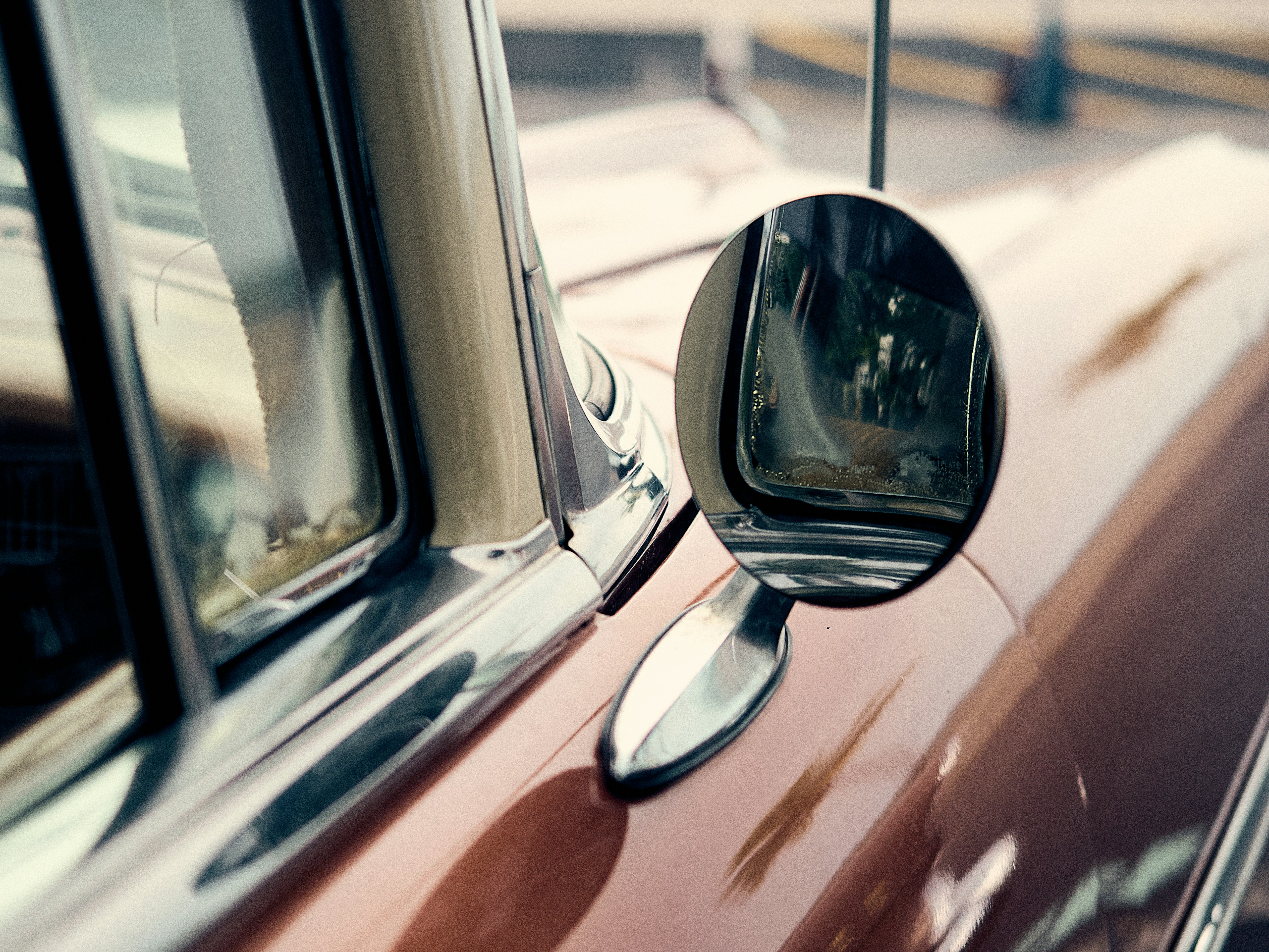 Close-up of a shiny chrome Volkswagen Beetle side mirror reflecting a sunny street