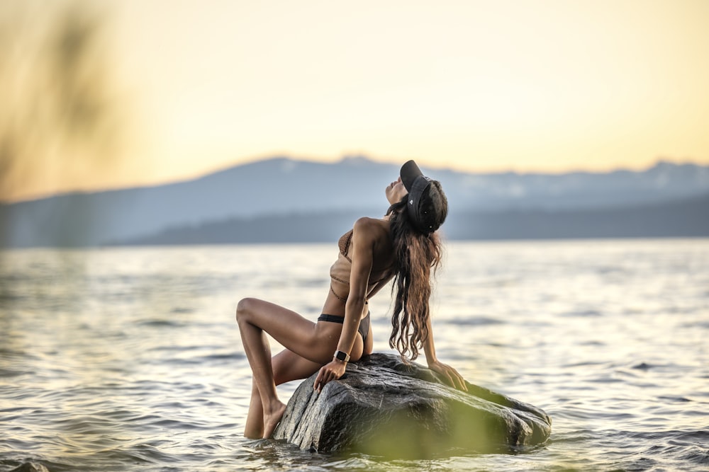a woman is sitting on a rock in the water