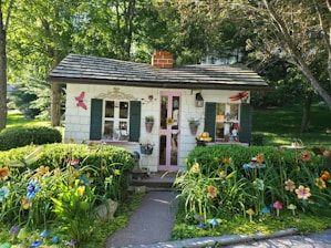 A cozy bungalow with a bright red door surrounded by blooming flowers on a sunny day.