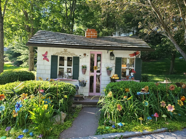 A cozy bungalow with a bright red door surrounded by blooming flowers on a sunny day.