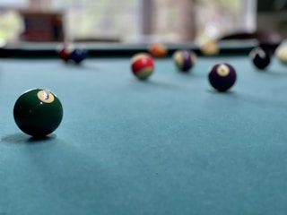 Close-up of a cocktail glass shimmering beside a pool table with colorful balls ready for a game.