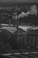 An archival black-and-white image of a bustling industrial site with workers and smokestacks under a cloudy sky.
