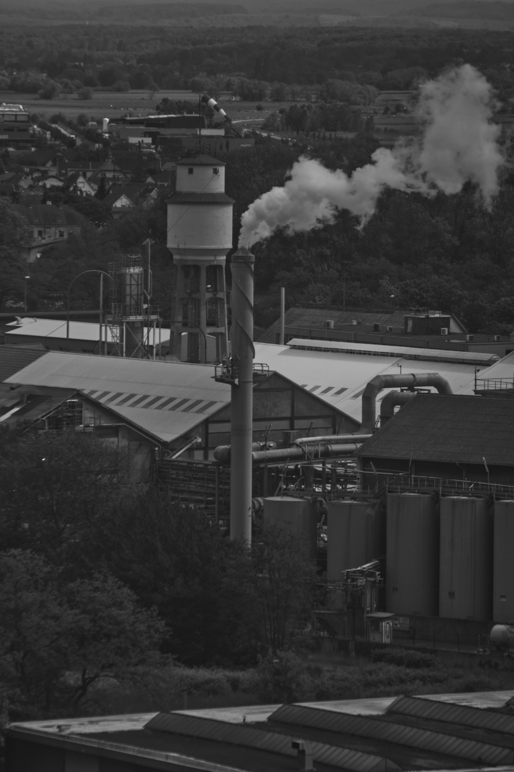 a black and white photo of a factory with smoke coming out of it