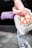 A person is holding a light-colored bag with peace symbols and the word 'Love.' The bag also contains a purple yoga mat. The individual is dressed in a pink long-sleeve shirt and floral-patterned leggings. The ground is made of gray pavement tiles, and there is a dark wall in the background.