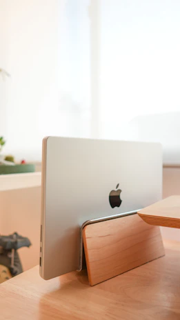 Ergonomic laptop stand carved from smooth, natural wood with soft olive background.