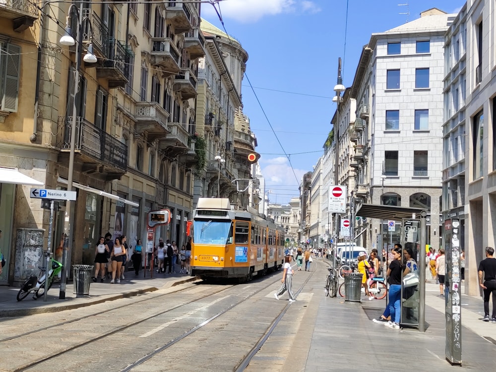 a yellow train traveling down a street next to tall buildings