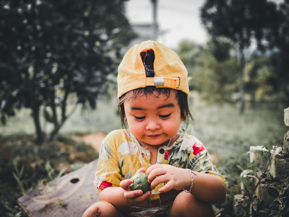 a small child wearing a yellow hat sitting on a log