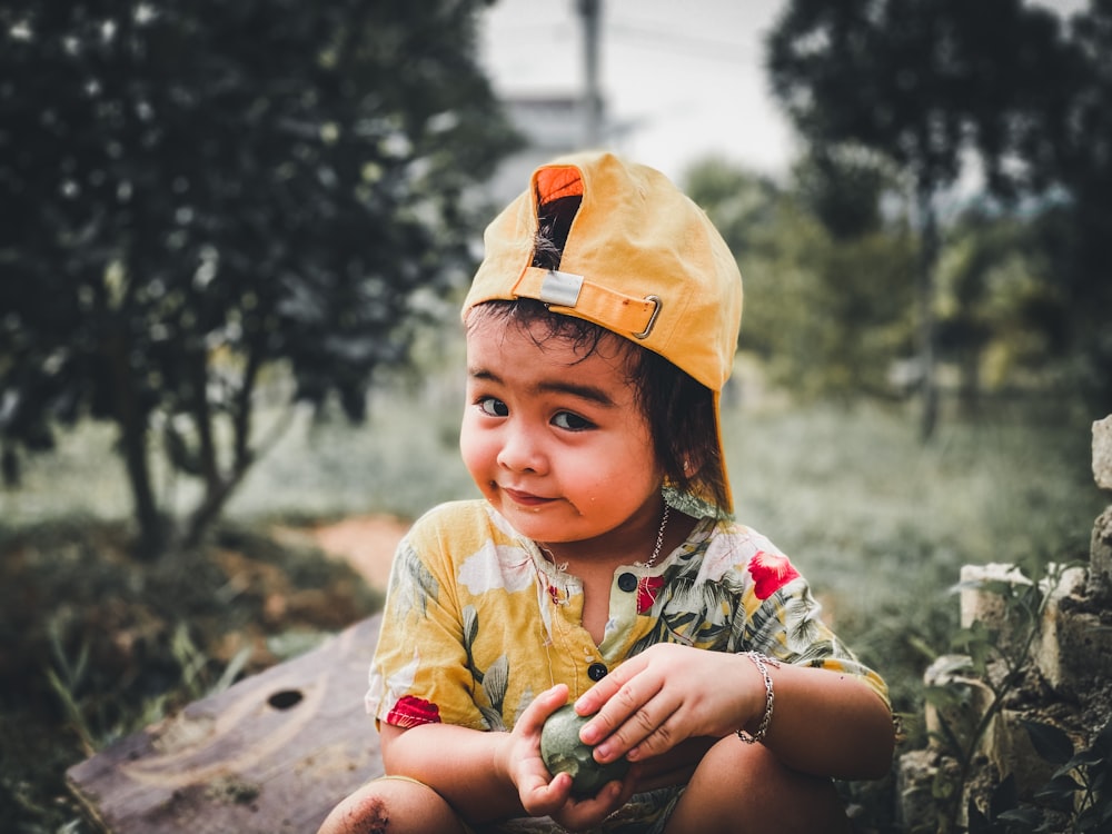 a little girl wearing a yellow hat sitting on a log