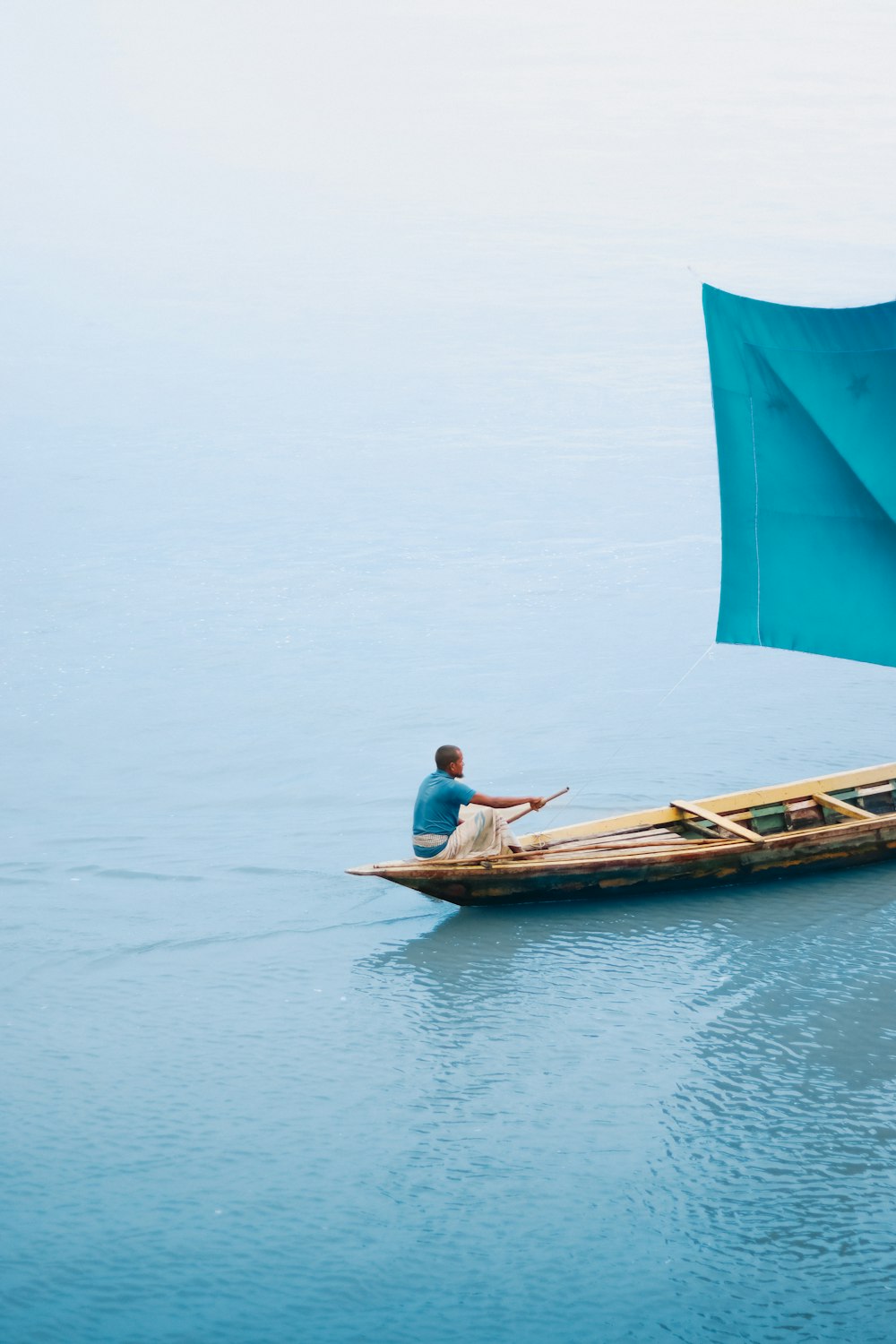 a man sitting in a boat with a blue sail