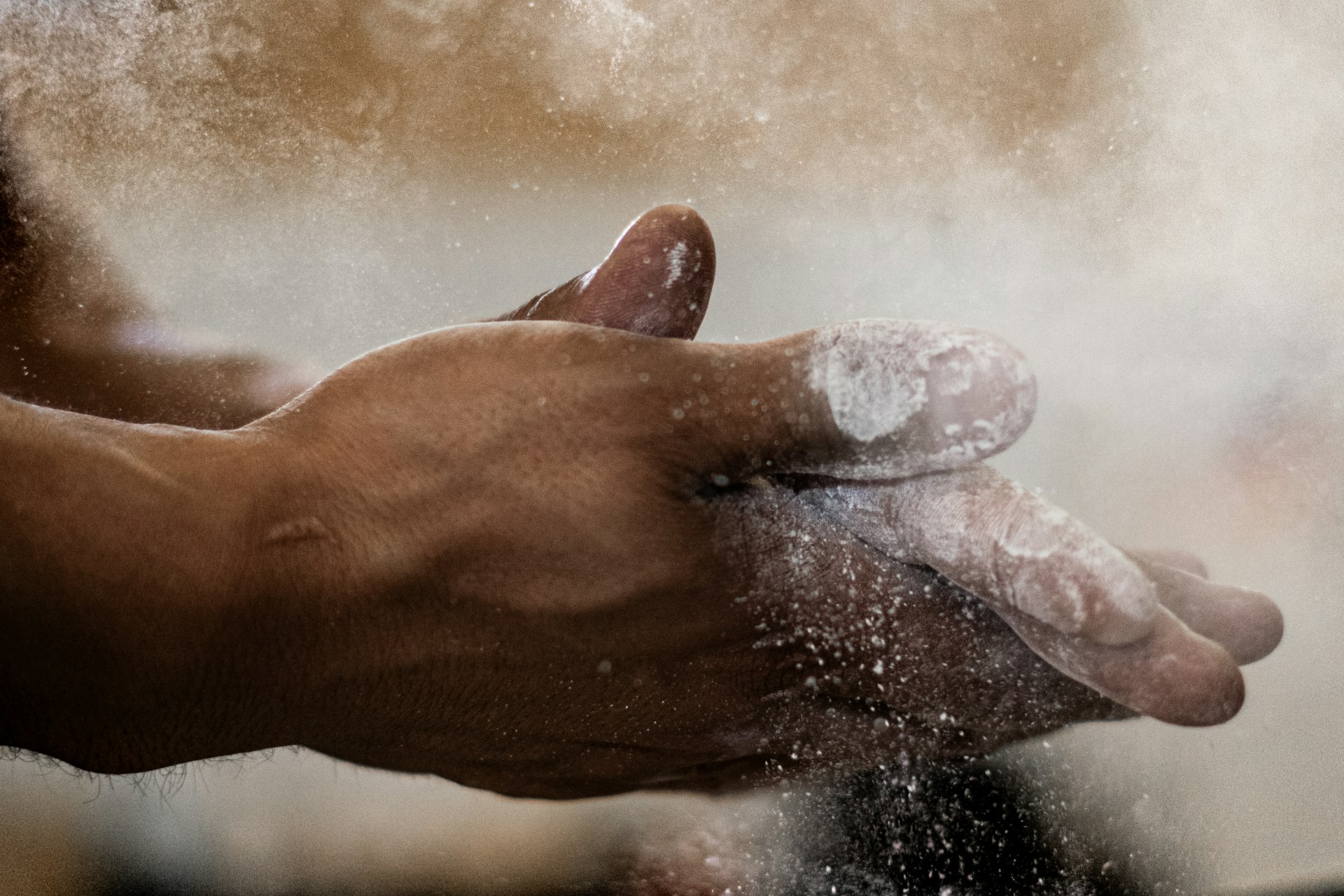 Athlete chalking both hands before a lift, chalk dust in the air