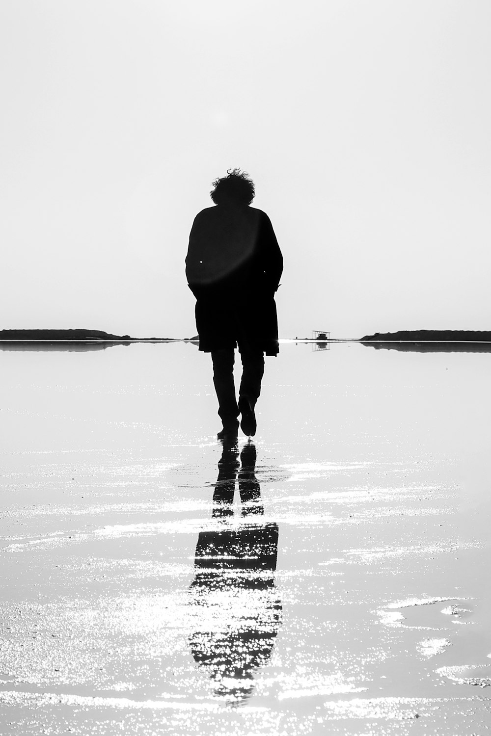 a black and white photo of a person walking on the beach