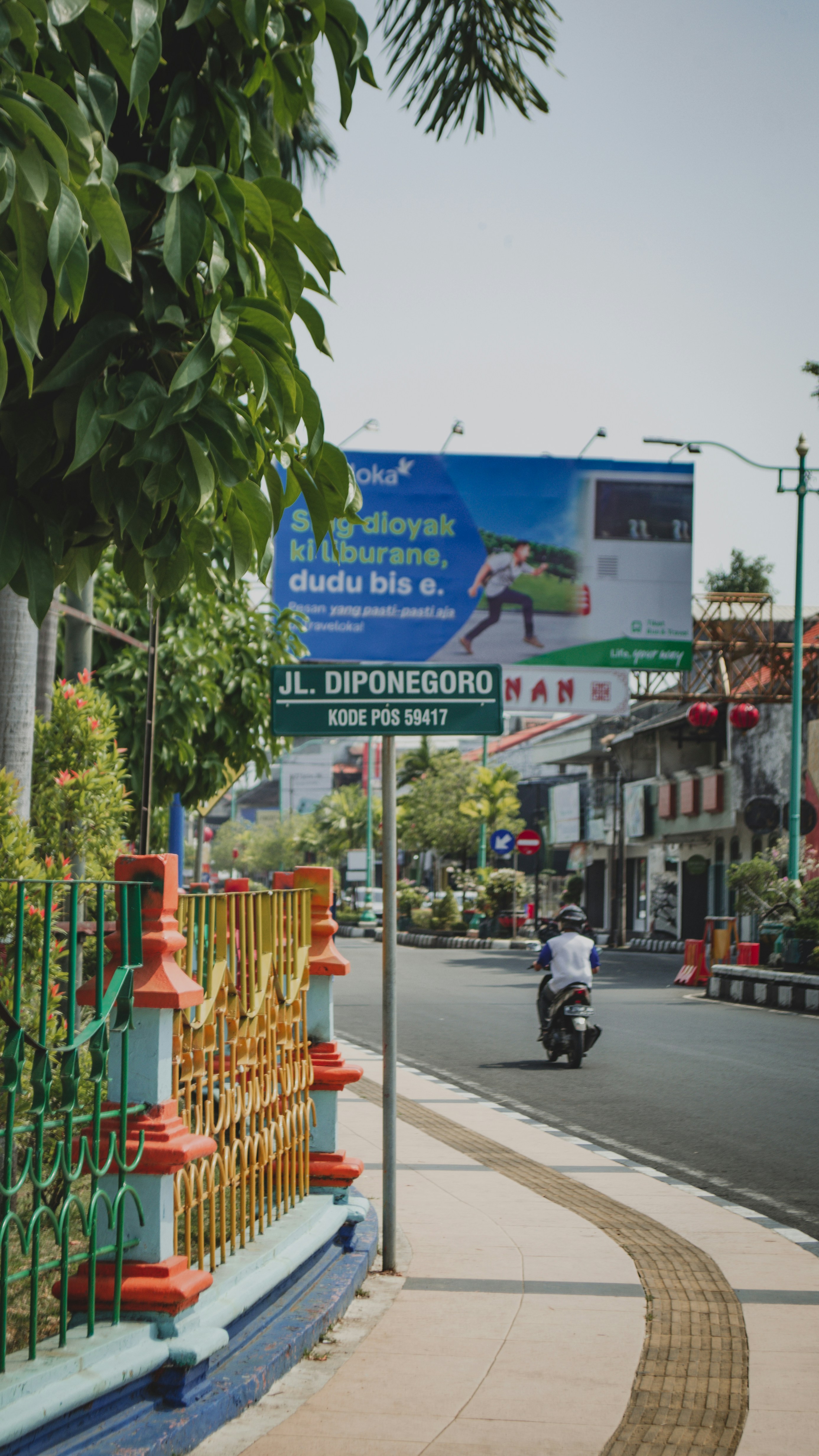 Seorang pria mengendarai sepeda motor di jalan di sebelah pagar