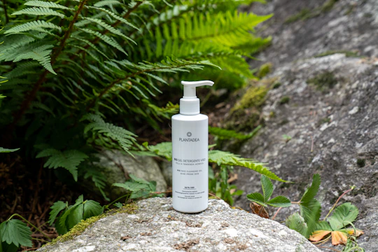 A sleek bottle of moisturizing cream surrounded by fresh green leaves on a marble countertop.