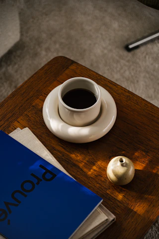Architectural plans spread out on a wooden table beside a cup of coffee, sunlight streaming in.