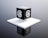 A black cube with a stylized letter 'a' in white on each visible face is placed on a raised white platform. The background is a gradient of gray, giving the scene a modern and minimalist aesthetic.