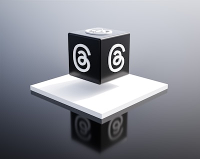 A black cube with a stylized letter 'a' in white on each visible face is placed on a raised white platform. The background is a gradient of gray, giving the scene a modern and minimalist aesthetic.