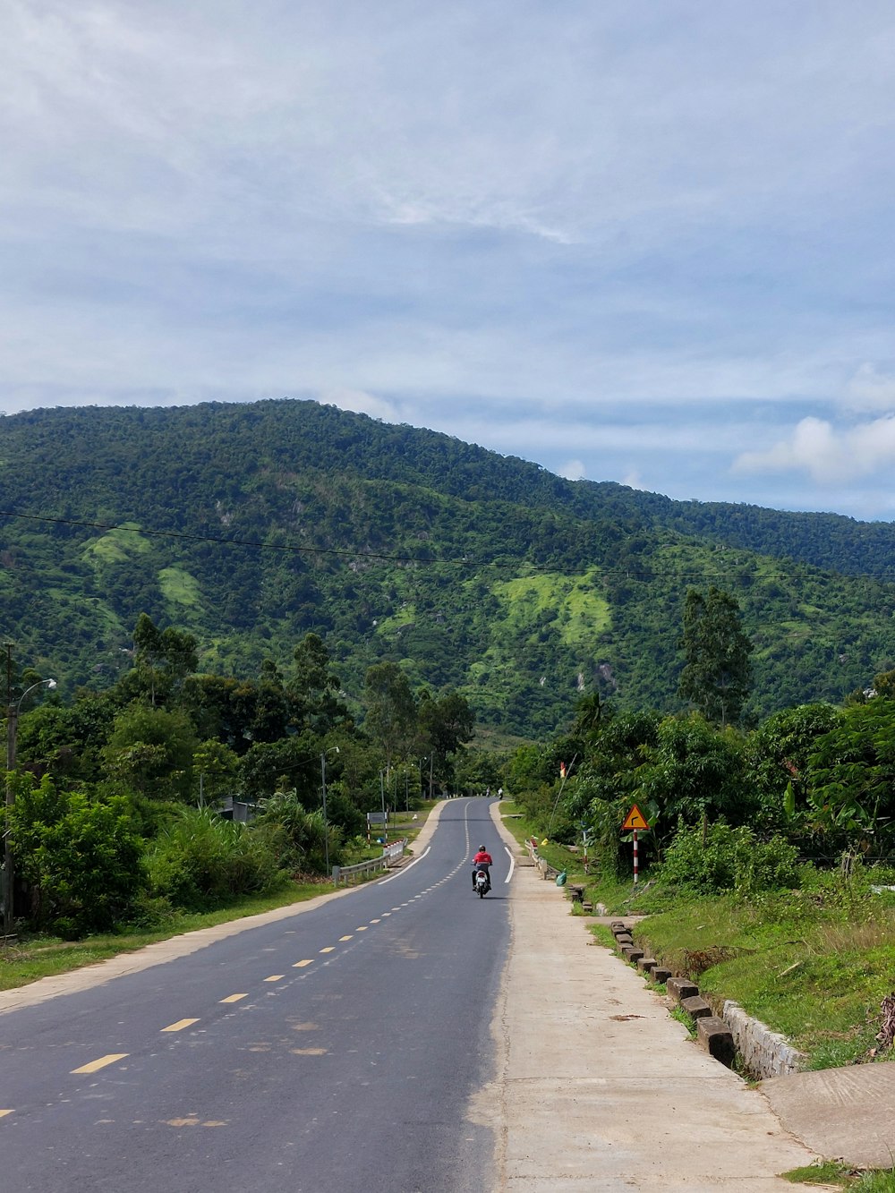 a man riding a motorcycle down a road next to a lush green hillside