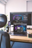 A workspace setup featuring an open laptop, smartphone, and large monitor displaying an interface for a meeting application. The environment includes a black chair visible in the foreground, a wooden desk, and a branded coffee cup. Light streams in from a window, illuminating a plant in the background.