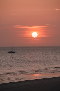 A serene sunrise over a calm ocean with a lone sailboat on the horizon.