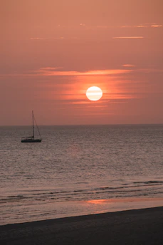 A serene sunrise over a calm ocean horizon with a lone sailboat.