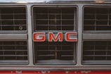 A close-up of a shiny GMC truck grill with a social media hashtag sticker on the bumper.