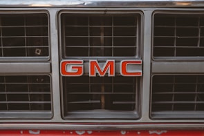A close-up of a shiny GMC truck grill with a social media hashtag sticker on the bumper.