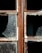 A close-up of a broken window with rusty metal frames. The glass is shattered, missing pieces, and covered in dust. The texture of the glass shows a honeycomb pattern, and the frame shows signs of wear and decay.