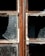 A close-up of a broken window with rusty metal frames. The glass is shattered, missing pieces, and covered in dust. The texture of the glass shows a honeycomb pattern, and the frame shows signs of wear and decay.