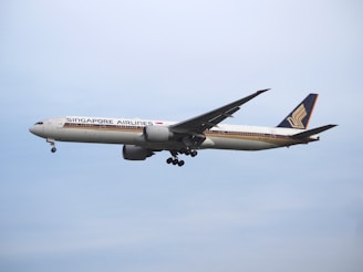 A large commercial airplane from Singapore Airlines is flying in the sky, showcasing its distinctive livery and logo on the fin. The aircraft appears to be in mid-flight with landing gear retracted, set against a clear blue sky.