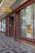 A sidewalk outside a building with large windows featuring vertical blinds and a sign on the window displaying the logo of 'Česká Pošta'. The building facade is constructed with brown and red brick, and a prominent yellow and blue 'POŠTA' sign hangs above the entrance.