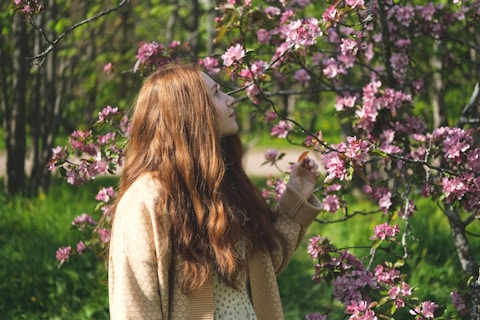 a woman standing in front of a tree with pink flowers