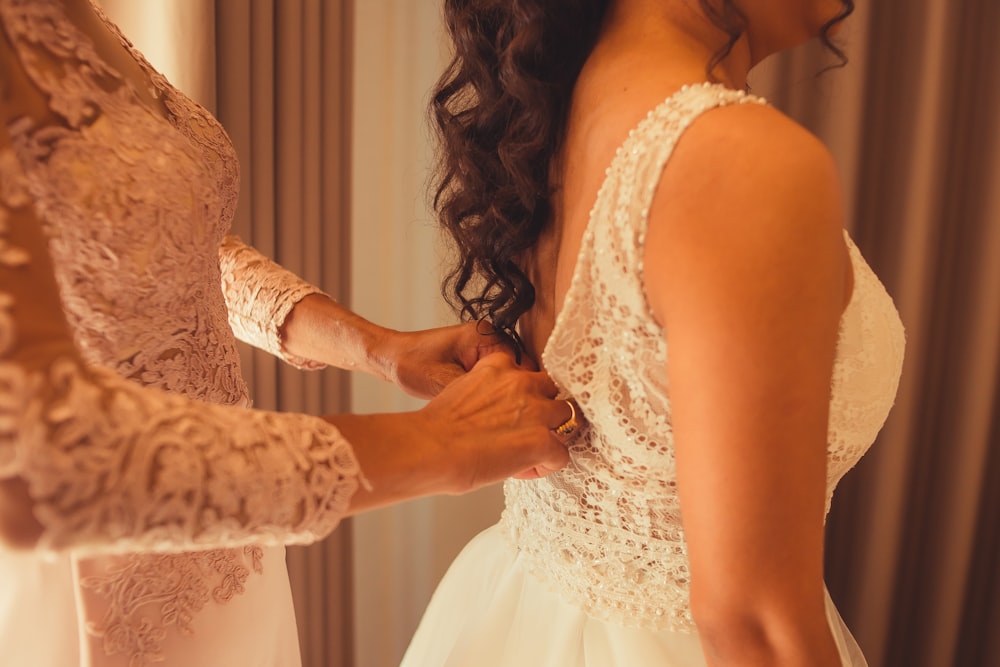 a woman is helping another woman put on her wedding dress