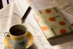 Warm coffee cup next to a notebook with delicate floral accents on a wooden table.
